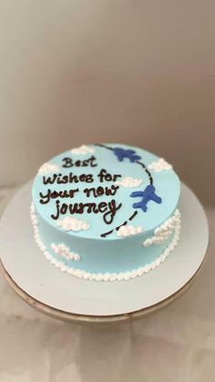 a blue and white cake with writing on it sitting on top of a table in front of a wall