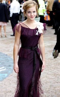 a woman in a purple dress is standing on the street with other people around her