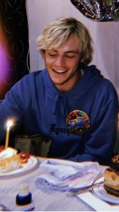 a man sitting at a table with two cakes on it and a lit candle in his mouth