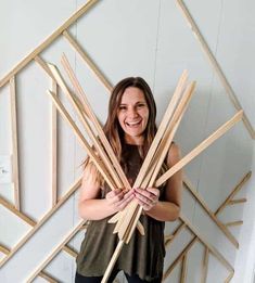 a woman standing in front of a white wall holding wooden sticks