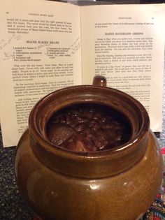 an open book sitting on top of a table next to a pot filled with food