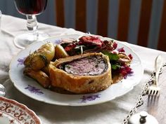 a white plate topped with meat and veggies next to a glass of wine