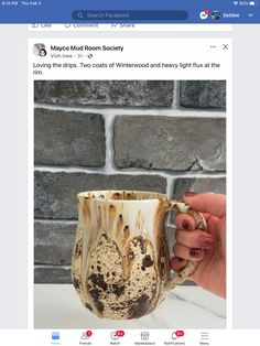 a person holding a coffee cup with brown and white designs on the inside, while it is in front of a brick wall