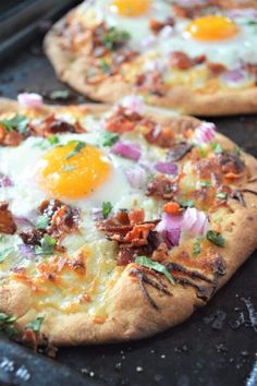 two pizzas sitting on top of a pan covered in cheese and bacon next to an egg