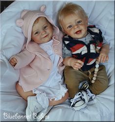 two baby dolls sitting next to each other on a bed