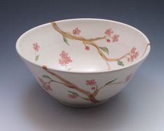 a white bowl with pink flowers and branches painted on the side, sitting on a gray surface