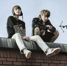 two young men sitting on top of a brick wall next to each other and looking off into the distance