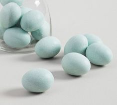 some blue and green colored rocks in a glass vase on a white surface with one sitting next to it