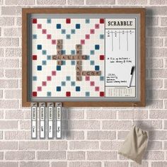 a scrabble board hanging on a brick wall next to four crayons