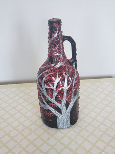 a red and white vase with trees painted on the front is sitting on a table