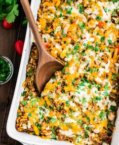 a casserole dish with meat, cheese and vegetables in it next to a wooden spoon