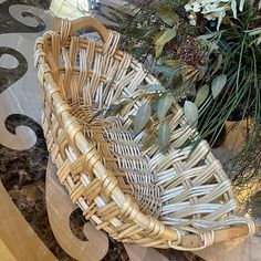 a wicker basket sitting on top of a marble floor next to flowers and greenery