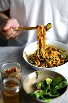 a person is eating noodles with chopsticks in a bowl next to some greens