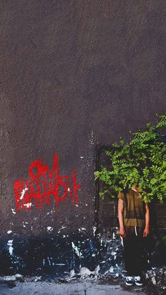 a man standing in front of a wall with graffiti on it and a tree growing out of his back