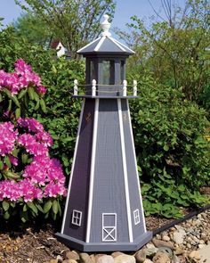 a small gray and white lighthouse sitting on top of a rock bed next to pink flowers