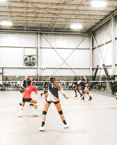 some girls are playing volleyball in an indoor court with other people watching from the sidelines