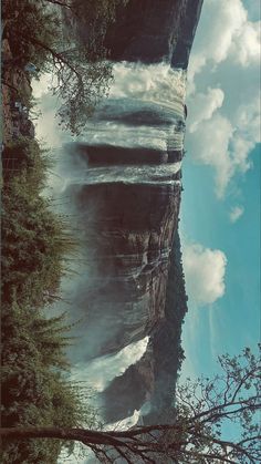 an image of a waterfall in the middle of some trees and sky with clouds above it