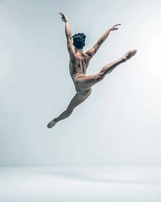 a male ballet dancer in the air with his arms extended and legs spread out,