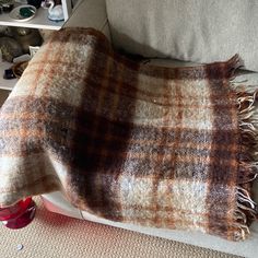 a brown and white plaid blanket sitting on top of a couch next to a red cup