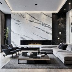 This luxurious living room exudes a striking contemporary aesthetic with its use of bold, dark tones and high-end materials. The focal point is the stunning marble fireplace wall, which creates a dramatic and eye-catching centerpiece. The plush, gray sectional sofa and complementary armchairs provide ample seating, while the low-profile wooden coffee table and sleek lighting fixtures contribute to the overall minimalist yet sophisticated vibe. The room is further enhanced by the contrast of the light wood floors and the dark marble and cabinetry, creating a beautifully balanced and visually captivating space. This design would be an inspiring inspiration for anyone seeking to create a modern, high-end living area in their home. Marble Fireplace Wall, Gray Sectional Sofa, Sleek Lighting, Luxurious Living Room, Dark Marble, Marble Fireplace, Light Wood Floors