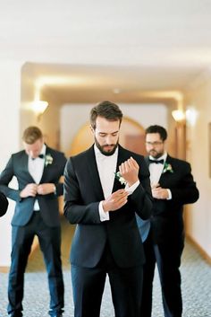 a man in a tuxedo is adjusting his tie while three other men stand behind him