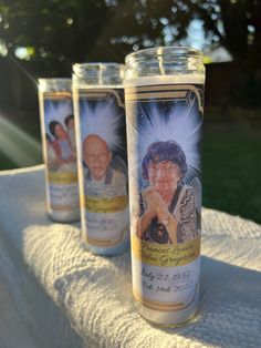 three candles with pictures of people on them sitting on a white table cloth in the sun