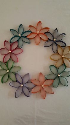 several different colored paper flowers arranged in a circle on a white surface with pearls attached to the petals