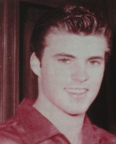 an old photo of a young man in a red shirt smiling at the camera with his hand on his hip