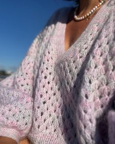 a woman wearing a pink sweater and pearls is holding a cell phone in her hand