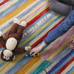 a person is playing with a stuffed monkey on the floor next to a colorful rug