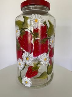 a glass vase with white daisies and strawberries painted on the side, sitting on a table