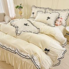 a white bed with black trim and ruffles in a room next to a window