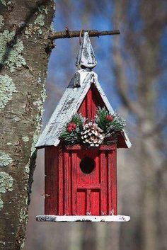 a red birdhouse hanging from a tree with pine cones on it's roof