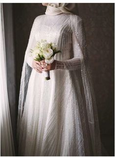 a woman in a white dress holding a bouquet of flowers and wearing a hijab