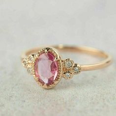 a gold ring with an oval shaped pink stone surrounded by small white diamonds on top