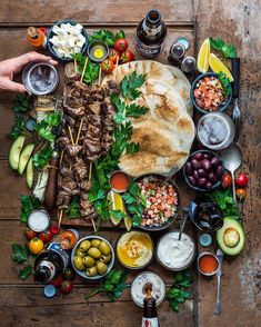 an assortment of food is laid out on a wooden table, including pita bread and olives