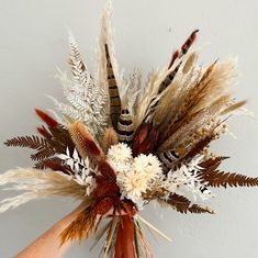 a hand holding a bouquet of dried flowers and feathers in it's centerpiece