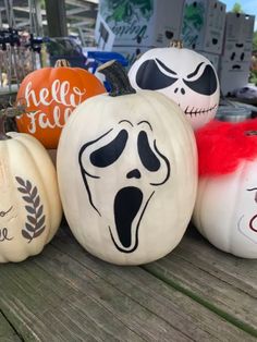 pumpkins with painted faces on them sitting on a wooden table in front of other pumpkins