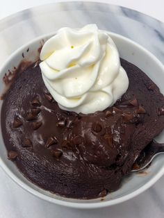 a chocolate dessert with whipped cream in a white bowl on a marble counter top,