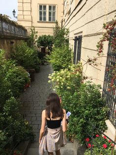 a woman is walking down the stairs in front of some plants and flowers on either side of her house