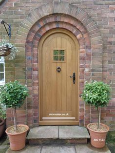 two potted plants sit in front of a wooden door on a brick building with an arched window