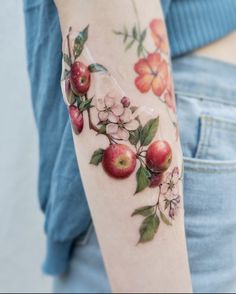 a woman's arm with an apple and flower tattoo on her left arm, in front of a blue shirt