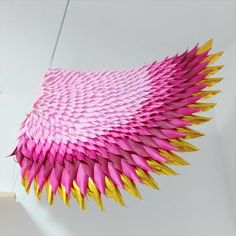 a pink and gold paper sculpture hanging from the ceiling in front of a white wall