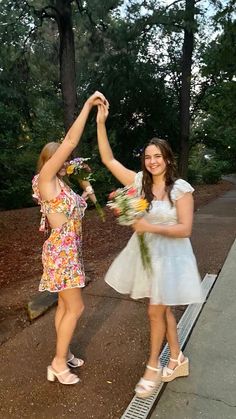 two young women are dancing together in the street while one holds flowers up to her chest