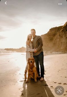 a man and woman standing on the beach with their dog