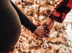 a pregnant woman holding the hand of a man in front of a decorated christmas tree