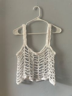 a white crocheted top hanging on a hanger next to a gray wall