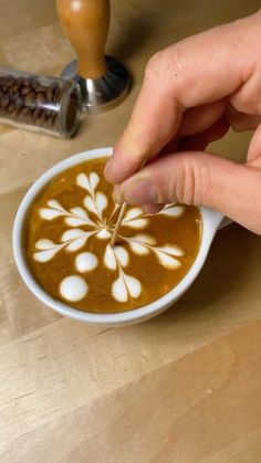 a person is dipping something into a cup of coffee with white designs on the foam