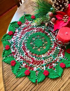 a crocheted doily on a wooden table with pine cones and red candles