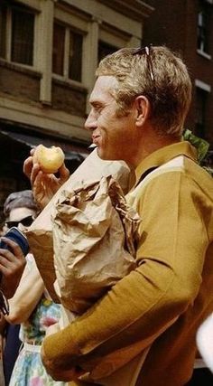 a man holding an apple in his right hand and wearing a paper bag around his neck